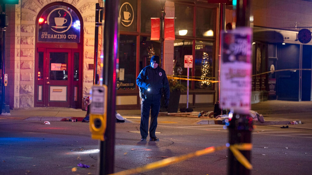 A police officer uses a flashlight while looking for evidence in downtown Waukesha, Wis., after an SUV sped through a barricade and slammed into a Christmas parade, injuring multiple people Sunday, Nov. 21, 2021. (AP Photo/Jeffrey Phelps)