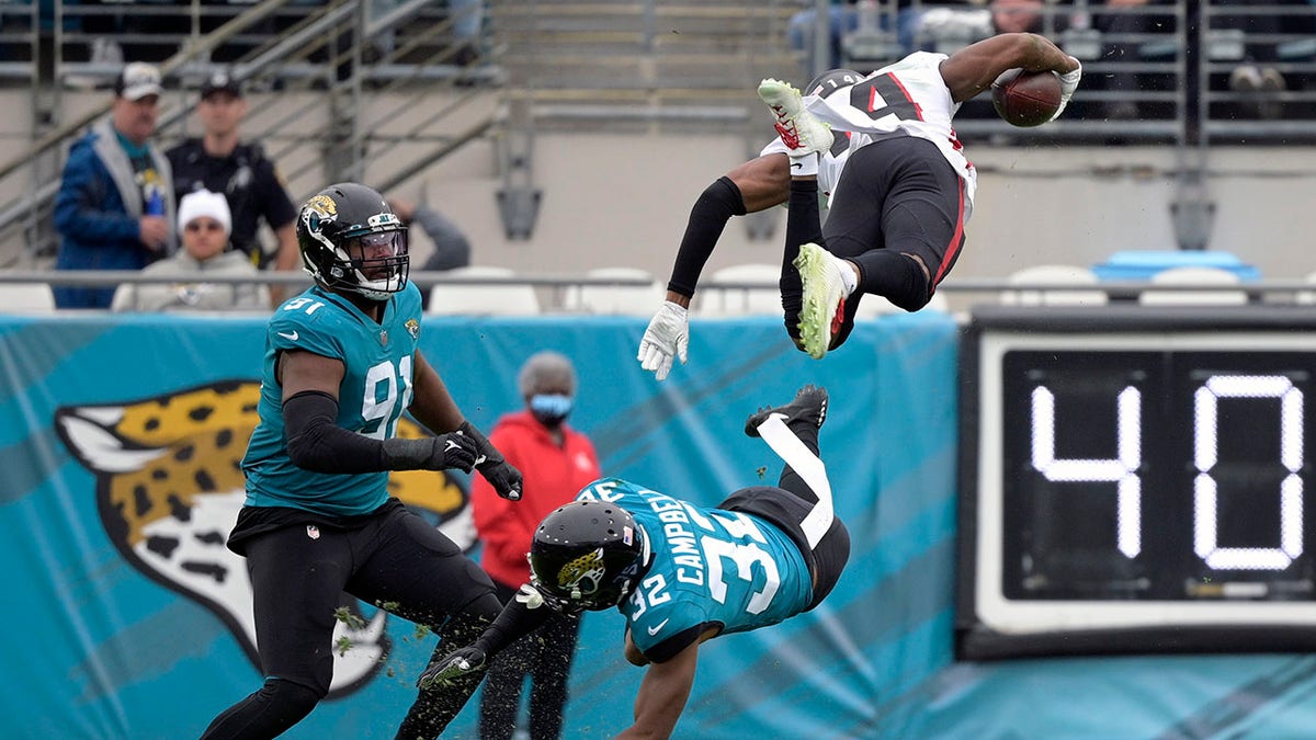 Atlanta Falcons wide receiver Russell Gage leaps over Jacksonville Jaguars cornerback Tyson Campbell and defensive end Dawuane Smoot after a reception Sunday, Nov. 28, 2021, in Jacksonville, Florida.