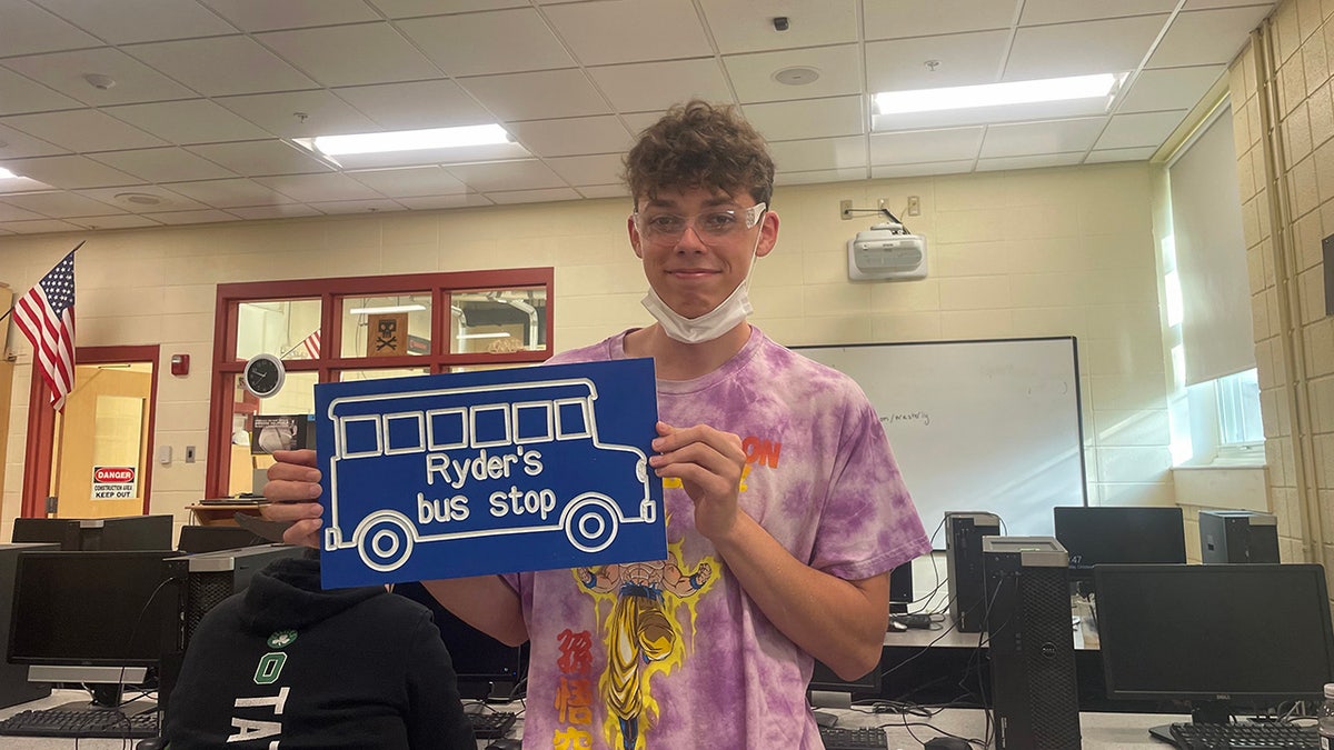 Student Mason Heald holding the sign that he designed and made for Ryder Killam's bus stop. 