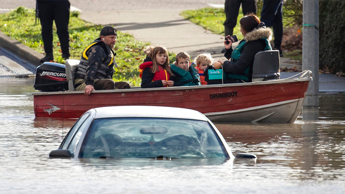 A woman and children who were stranded by high water due to flooding are rescued by a volunteer operating a boat as another person's car is submerged near them in Abbotsford, British Columbia, on Tuesday, Nov. 16, 2021.