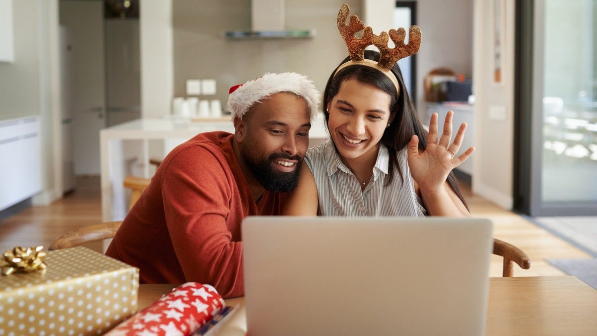 Two people wearing Christmas attire waving on video call