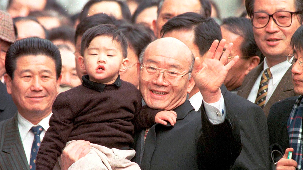 Former South Korean Presidnt Chun Doo-hwan, holding his grandson, waves to his supporters and neighbors upon his arrival at home after being released from prison in a special government amnesty on Dec. 22, 1997. 