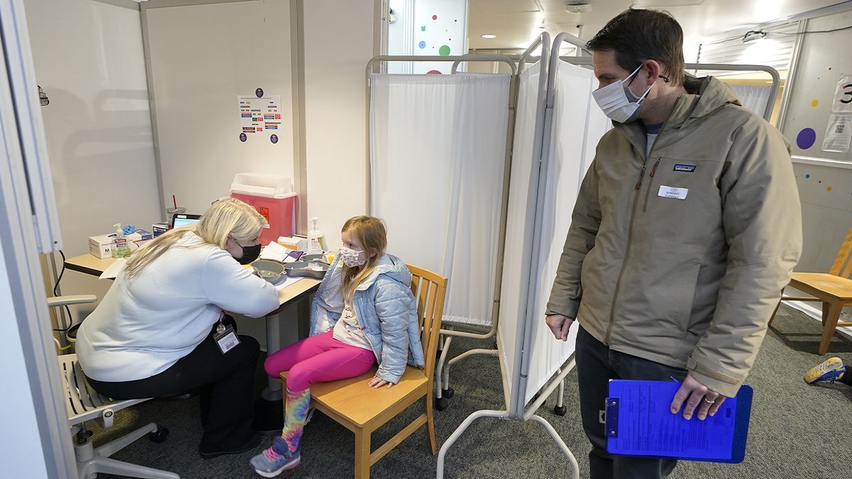 Shauna Andrus, left, a nurse volunteering at the University of Washington Medical Center, talks to Emmy Slonecker, 7, center, before giving her the first shot of the Pfizer COVID-19 vaccine on Tuesday as Emmy's father, Brent Slonecker, right, looks on in Seattle.