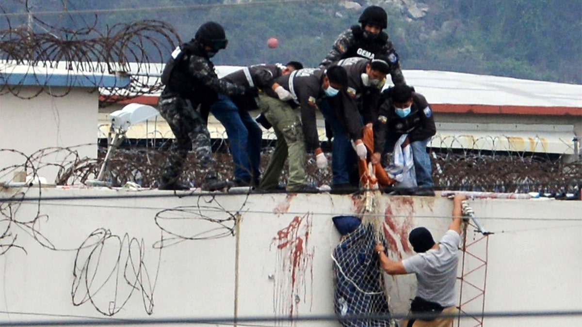 Police lower the body of a prisoner from the roof of the Litoral penitentiary the morning after riots broke out inside the jail in Guayaquil, Ecuador, Saturday, Nov. 13, 2021. (AP Photo/Jose Sanchez)