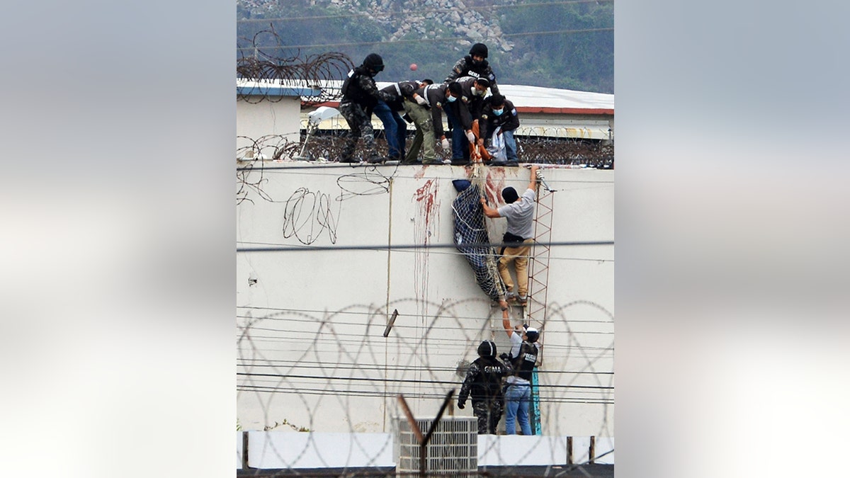 Police lower the body of a prisoner from the roof of the Litoral penitentiary the morning after riots broke out inside the jail in Guayaquil, Ecuador, Saturday, Nov. 13, 2021.