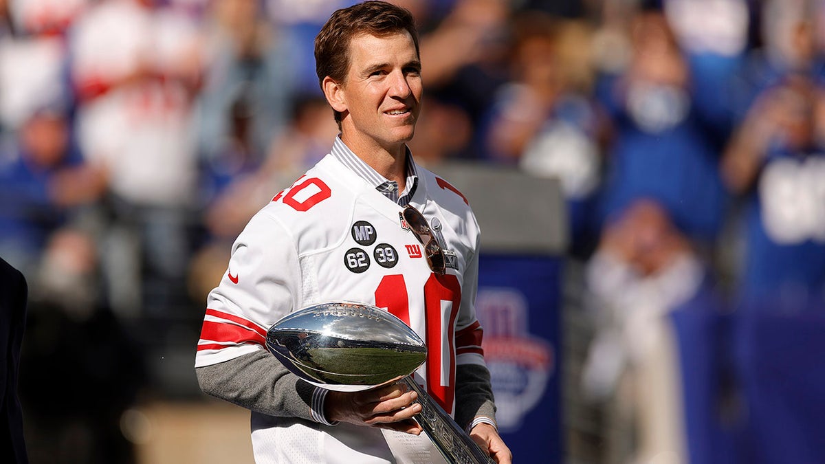 Former New York Giants quarterback Eli Manning walks onto the field carrying the Vince Lombardi Trophy during a ceremony honoring the 2011 Giants Super Bowl team at halftime during a game against the Los Angeles Rams at MetLife Stadium on October 17, 2021 in East Rutherford, New Jersey.