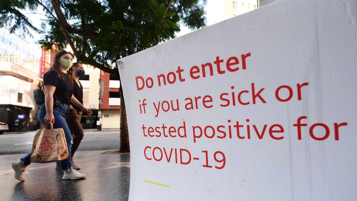 Pedestrians wearing facemasks walk past a sign posting Covid-19 requirements in front of a store in Hollywood, California on November 2, 2021. (Photo by Frederic J. BROWN / AFP) (Photo by FREDERIC J. BROWN/AFP via Getty Images)