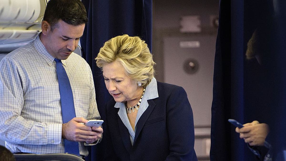 Democratic presidential nominee Hillary Clinton looks at a smart phone with national press secretary Brian Fallon on her plane at Westchester County Airport October 3, 2016 in White Plains, New York. (Photo credit: BRENDAN SMIALOWSKI/AFP via Getty Images)