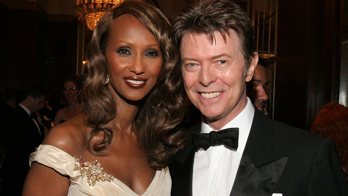 Iman wearing an off the shoulder dress smiling with David Bowie