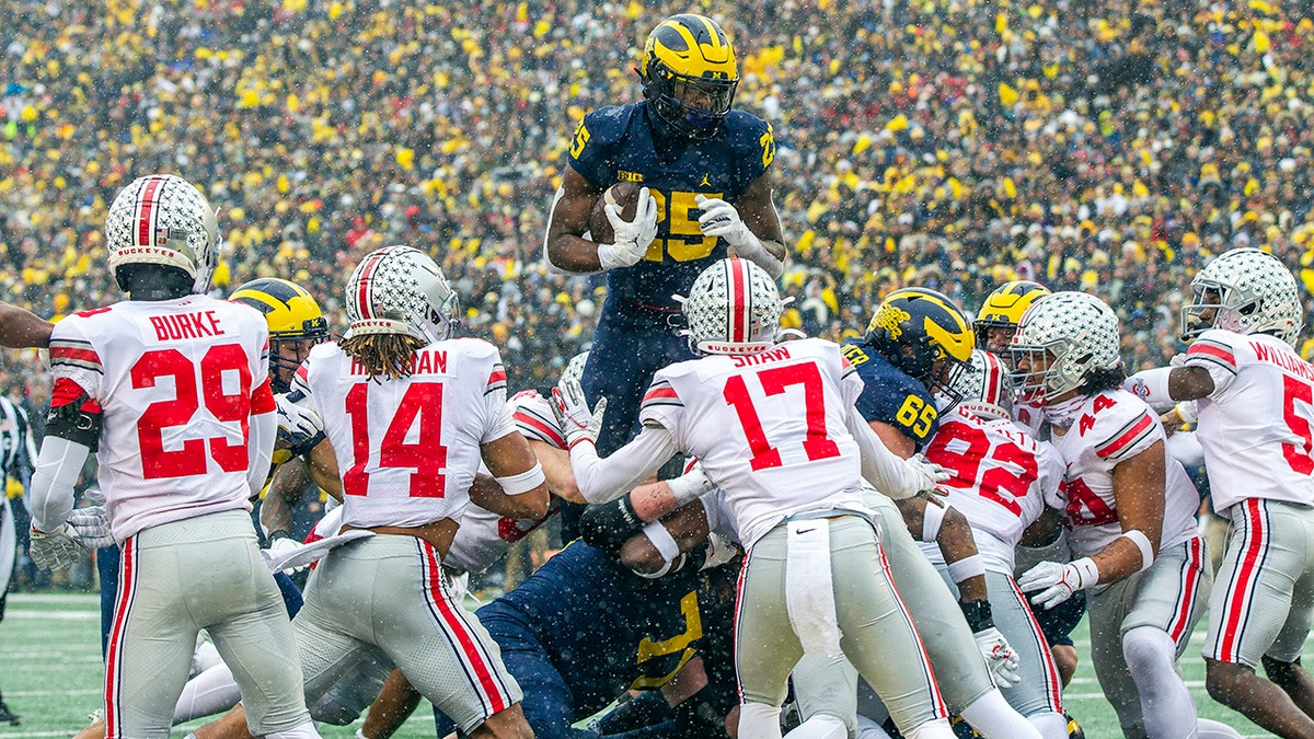 Michigan running back Hassan Haskins (25) leaps over Ohio State defenders for a touchdown in the second quarter of an NCAA college football game in Ann Arbor, Mich., Saturday, Nov. 27, 2021.