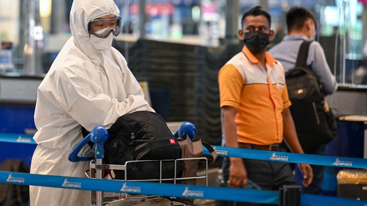 A passenger wearing personal protective equipment queues to check-in for a flight at the Kuala Lumpur International Airport on Nov. 29, 2021, as countries across the globe shut borders and renewed travel curbs in response to the spread of a new, heavily mutated COVID-19 coronavirus variation. 
