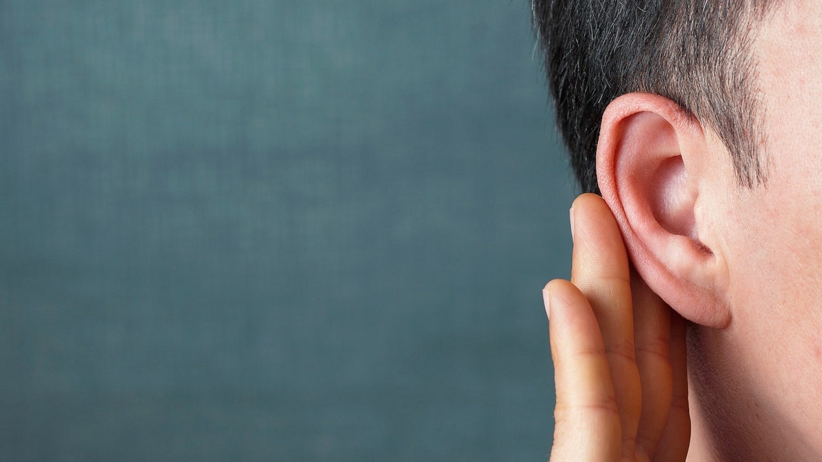 The man listens attentively with her palm to her ear, close up