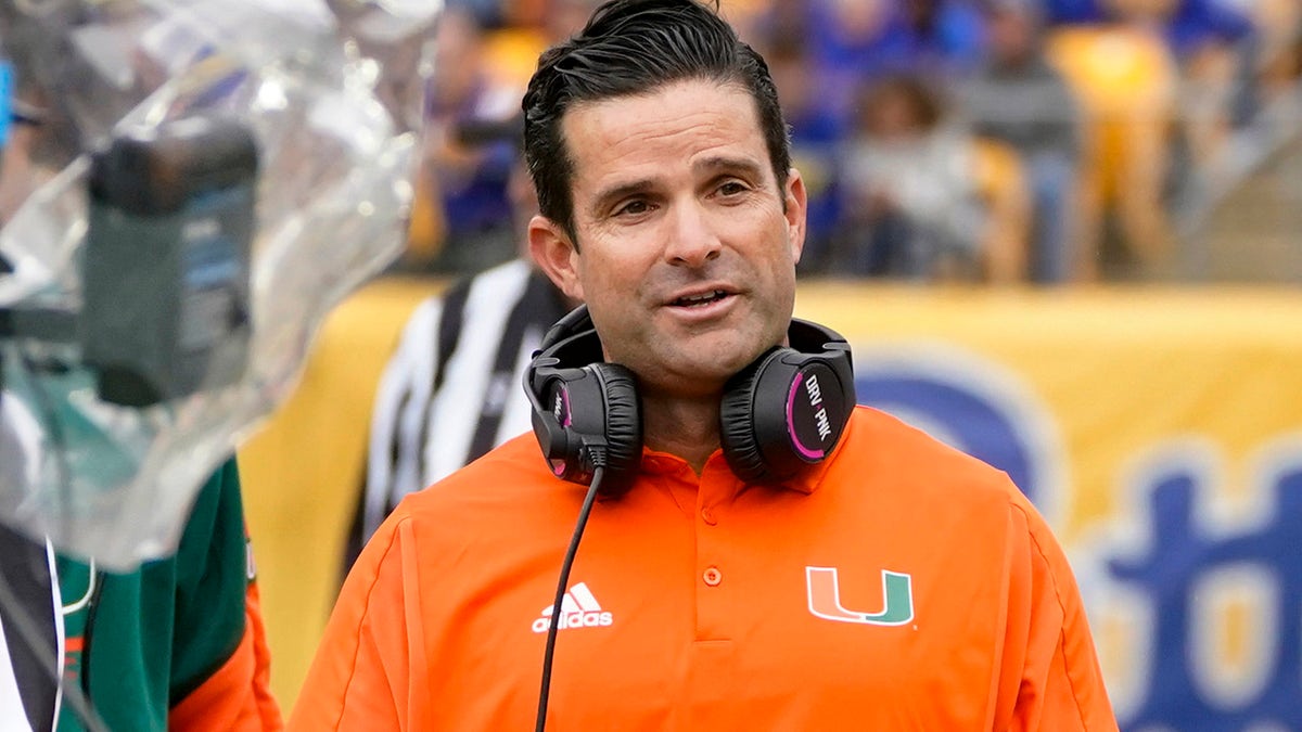 Miami head coach Manny Diaz, right, watches as referee Jeff Heaser, left, looks at a review screen after a targeting penalty was called against Miami during the first half of an NCAA college football game, Saturday, Oct. 30, 2021, in Pittsburgh. The review determined no targeting.