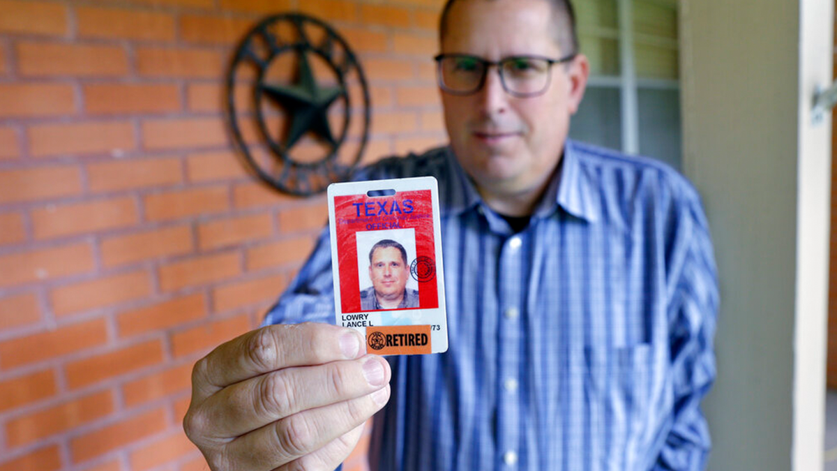 Lance Lowry, a recently retired corrections officer with the Texas State Penitentiary, holds his ID badge on the front porch of his home, Oct. 27, 2021, in Huntsville, Texas.