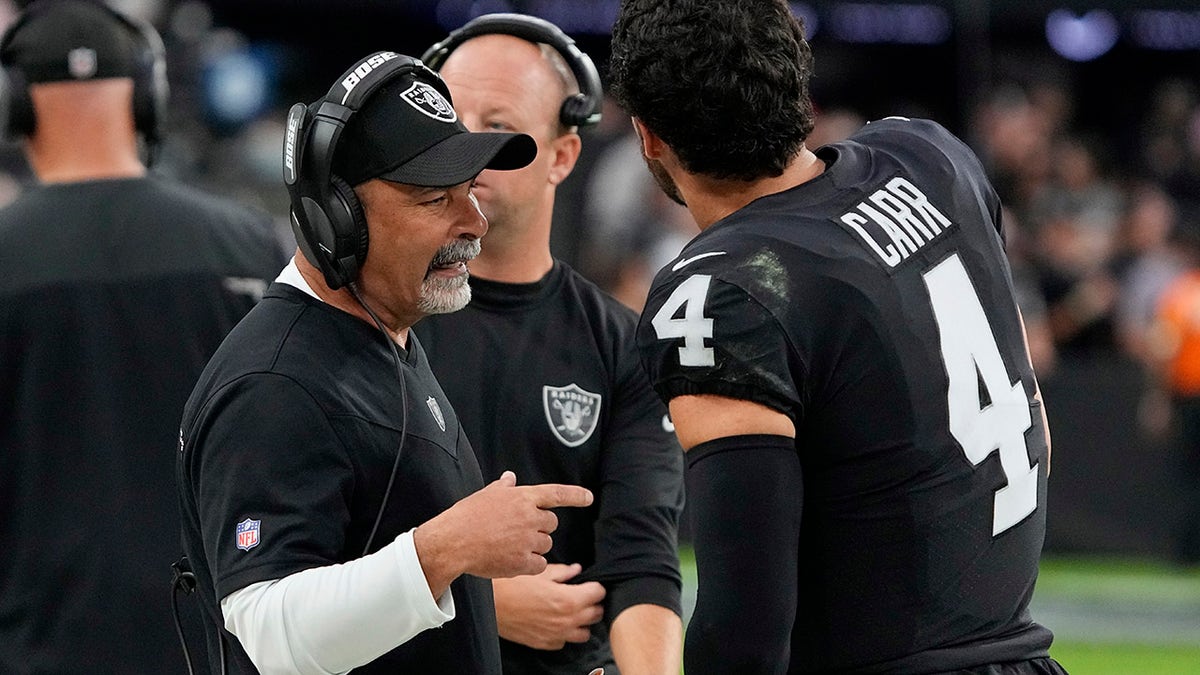 Las Vegas Raiders interim head coach Rich Bisaccia speaks with quarterback Derek Carr (4) during the second half of an NFL football game against the Philadelphia Eagles, Sunday, Oct. 24, 2021, in Las Vegas.