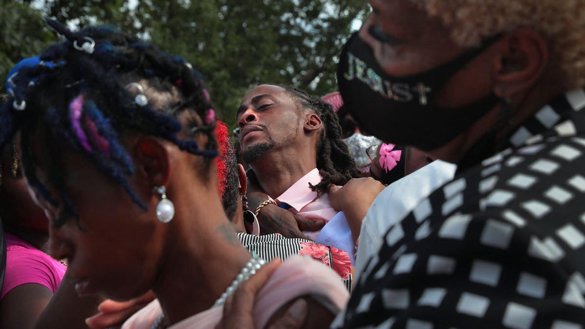 Deontae Davis Sr. is hugged at rear as Elder Carolyn Rice-Smith, right, supports Sabrina Dunigan at the end of burial services for their children at Sunset Gardens of Memory Cemetery in Millstadt, Illinois in August 2021. 