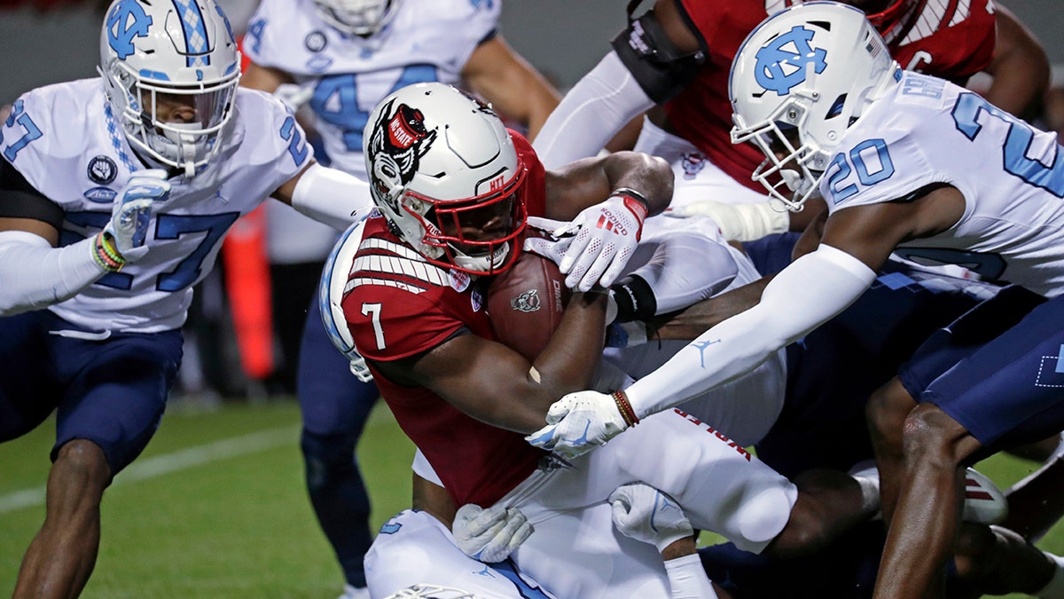 North Carolina State running back Zonovan Knight (7) gets tackled by North Carolina defensive back Giovanni Biggers (27) and defensive back Tony Grimes (20) during the first half of an NCAA college football game Friday, Nov. 26, 2021, in Raleigh, North Carolina.