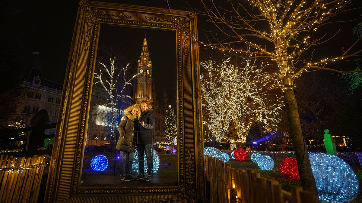 A couple poses for a photograph backdropped by the building of the city hall at a Christmas market in Vienna, Austria, Sunday, Nov. 21, 2021. 