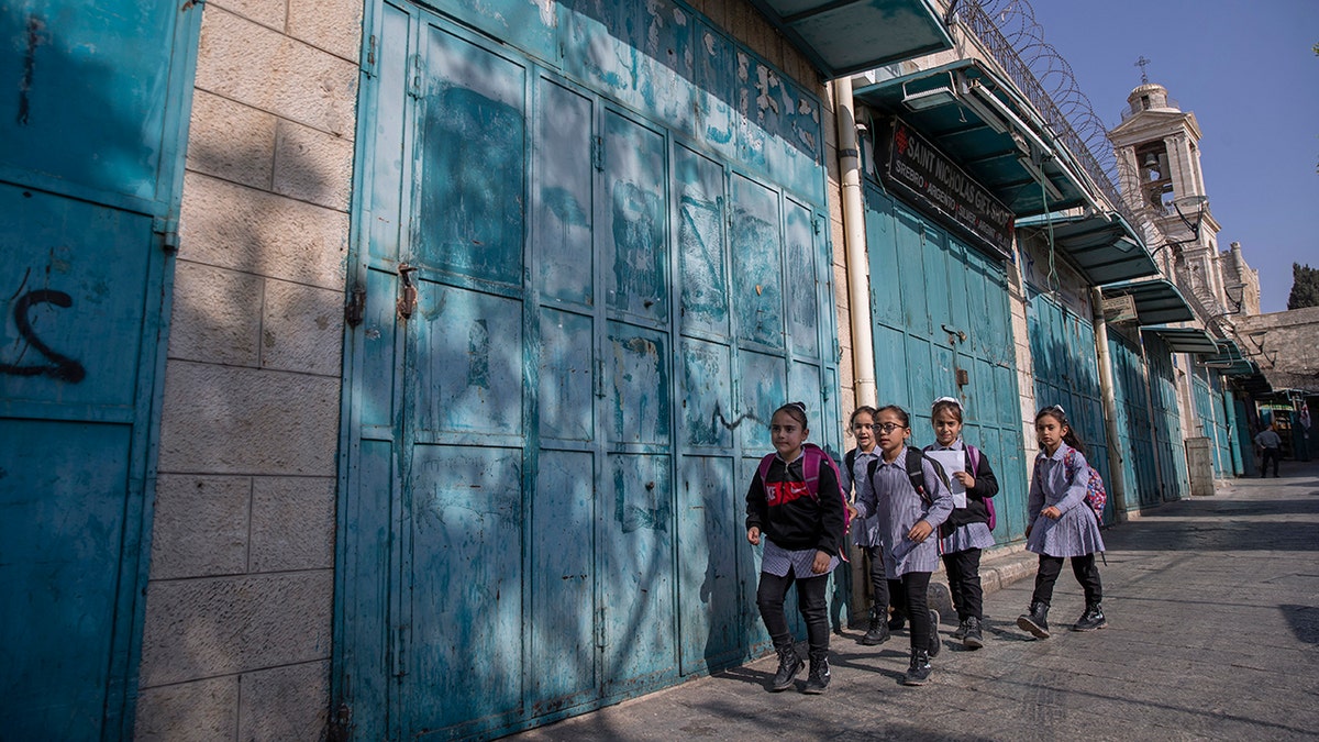 Palestinian children walk past closed souvenir shops at the tourists market adjacent to the Church of the Nativity, in the West Bank city of Bethlehem, Tuesday, Nov. 16, 2021. 