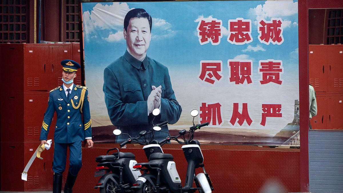 A Chinese honor guard member walks past a poster of Chinese leader Xi Jinping near the entrance to the Forbidden City in Beijing on Sept. 18, 2021.  President Xi has been absent from the Group of 20 summit in Rome and global climate talks in Scotland, drawing criticism from U.S. President Biden and questions about China’s commitment to reducing greenhouse gas emissions.  