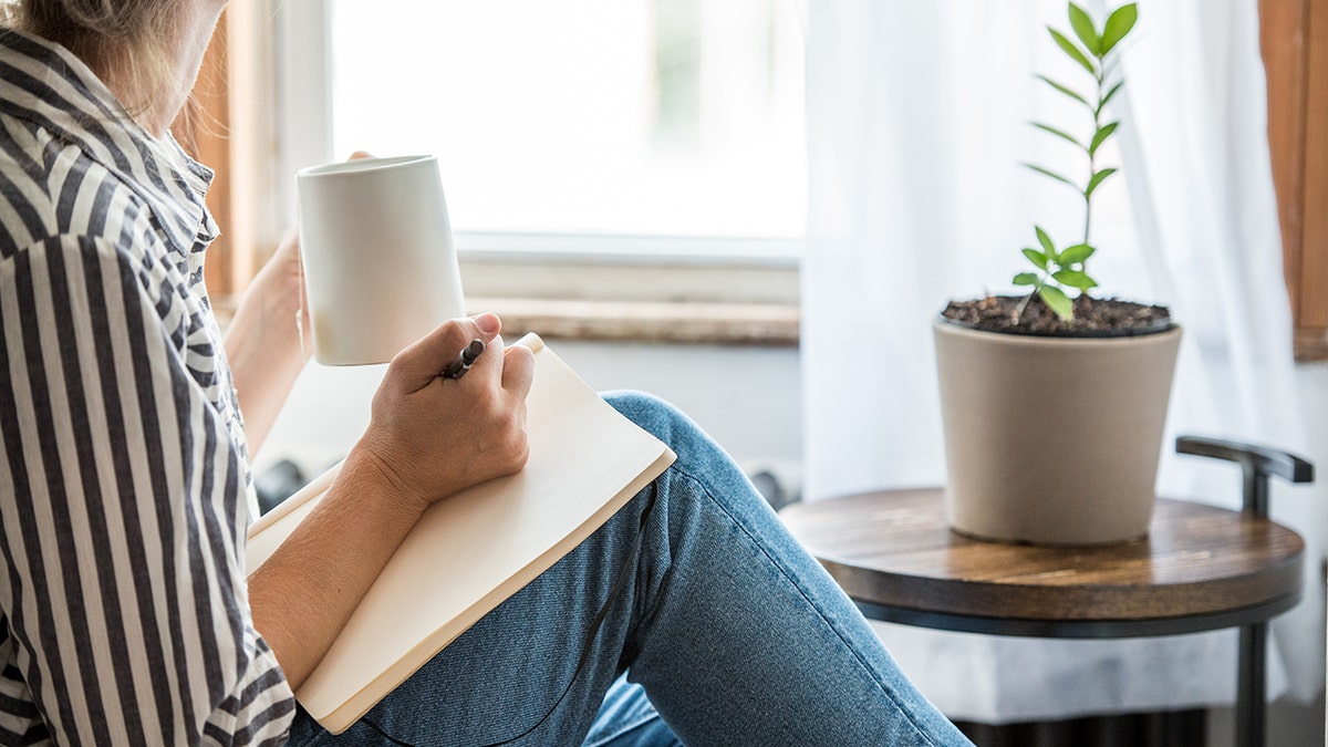 Person writing in journal holding mug