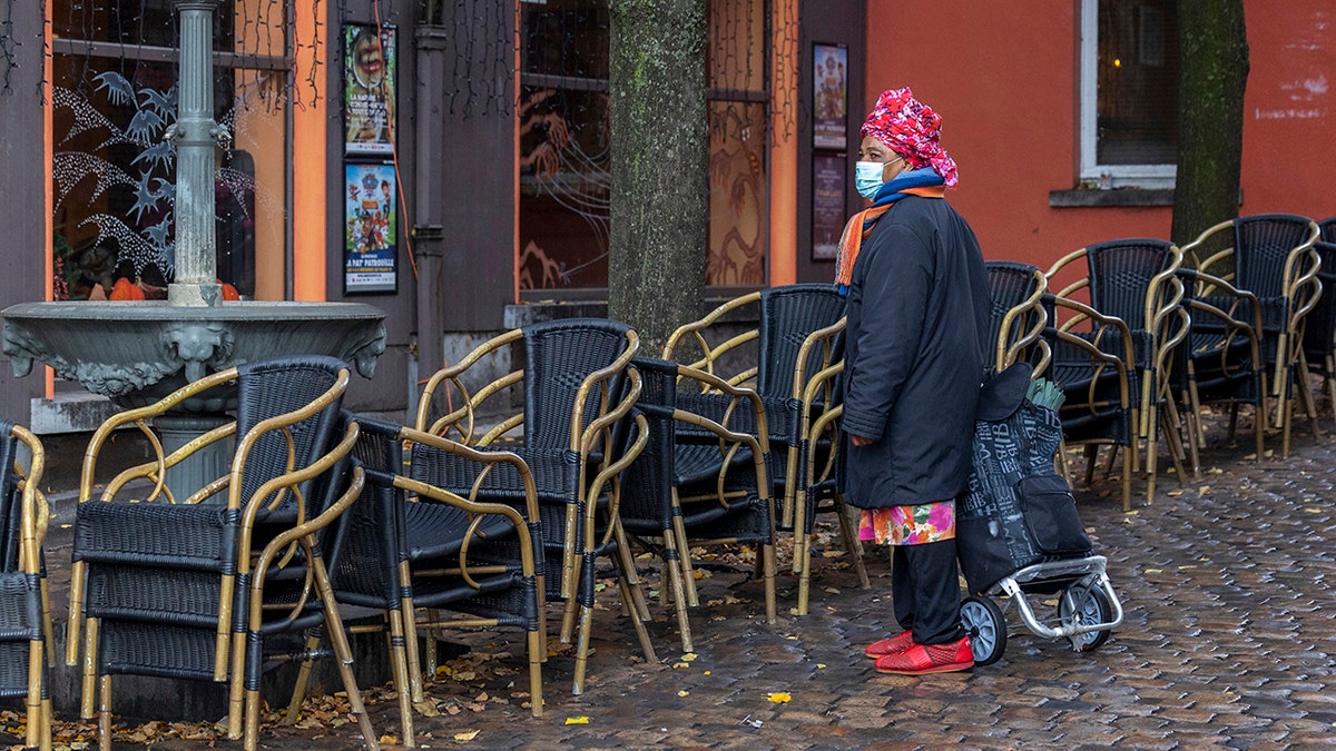 A woman wears a face mask to protect herself against the coronavirus as she passes by an empty terrace in the Marrolles quarter in Brussels, Belgium, Nov. 17, 2021.