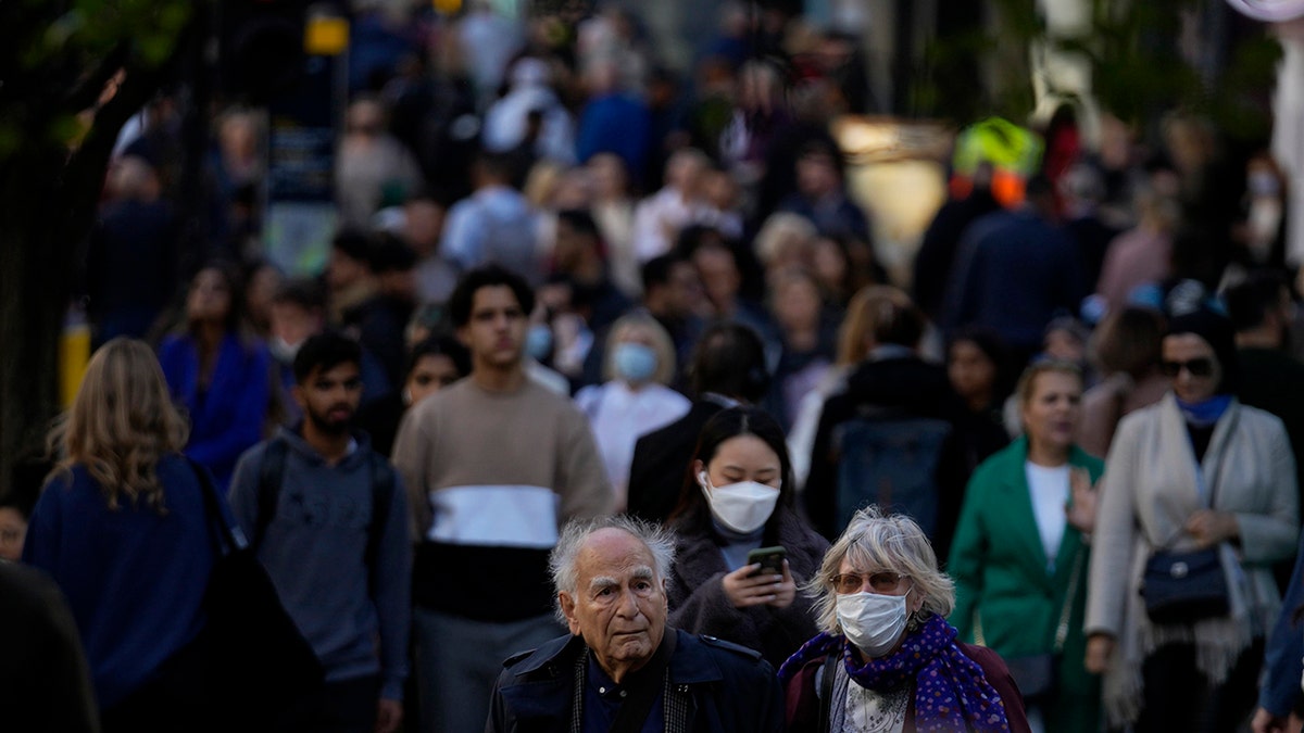 People wearing face masks walk along the Oxford Street shopping area of central London, Oct. 20, 2021. 