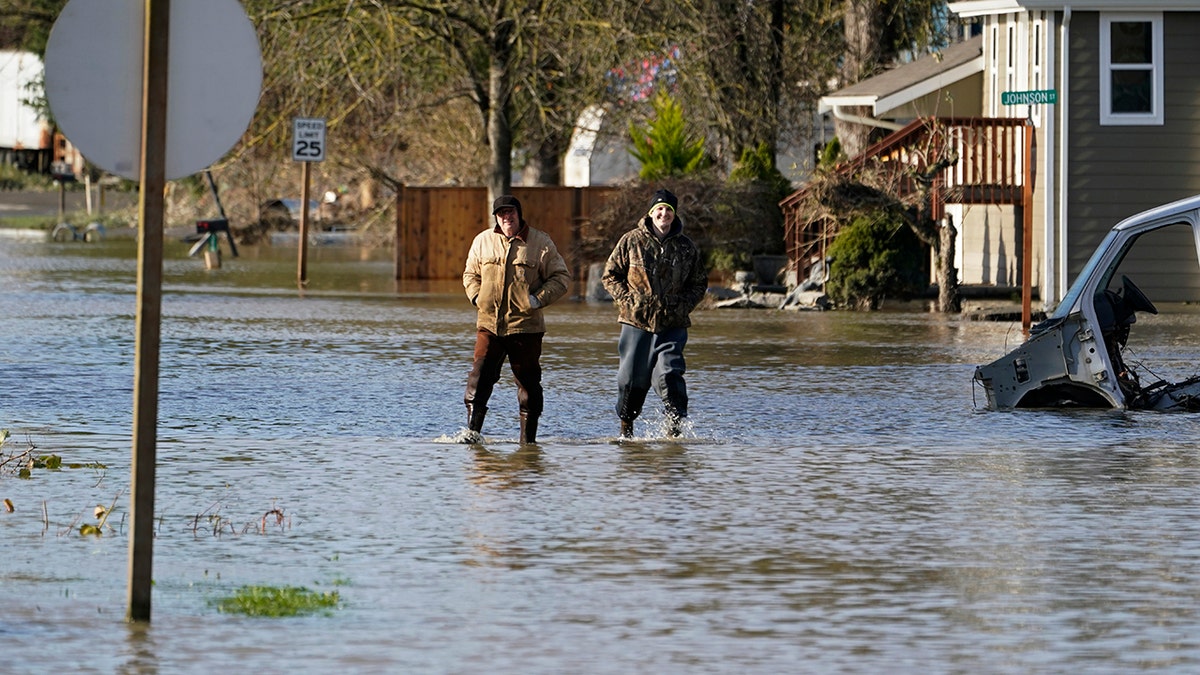 People walk through floodwaters Wednesday, Nov. 17, 2021, in Sumas, Washington. 