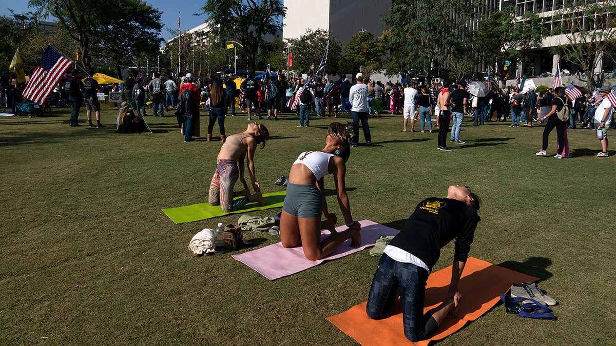 Three women practice yoga to "peacefully" protest the city's new vaccine mandate at a rally in Los Angeles Monday, Nov. 8, 2021, in Los Angeles. (AP Photo/Jae C. Hong)