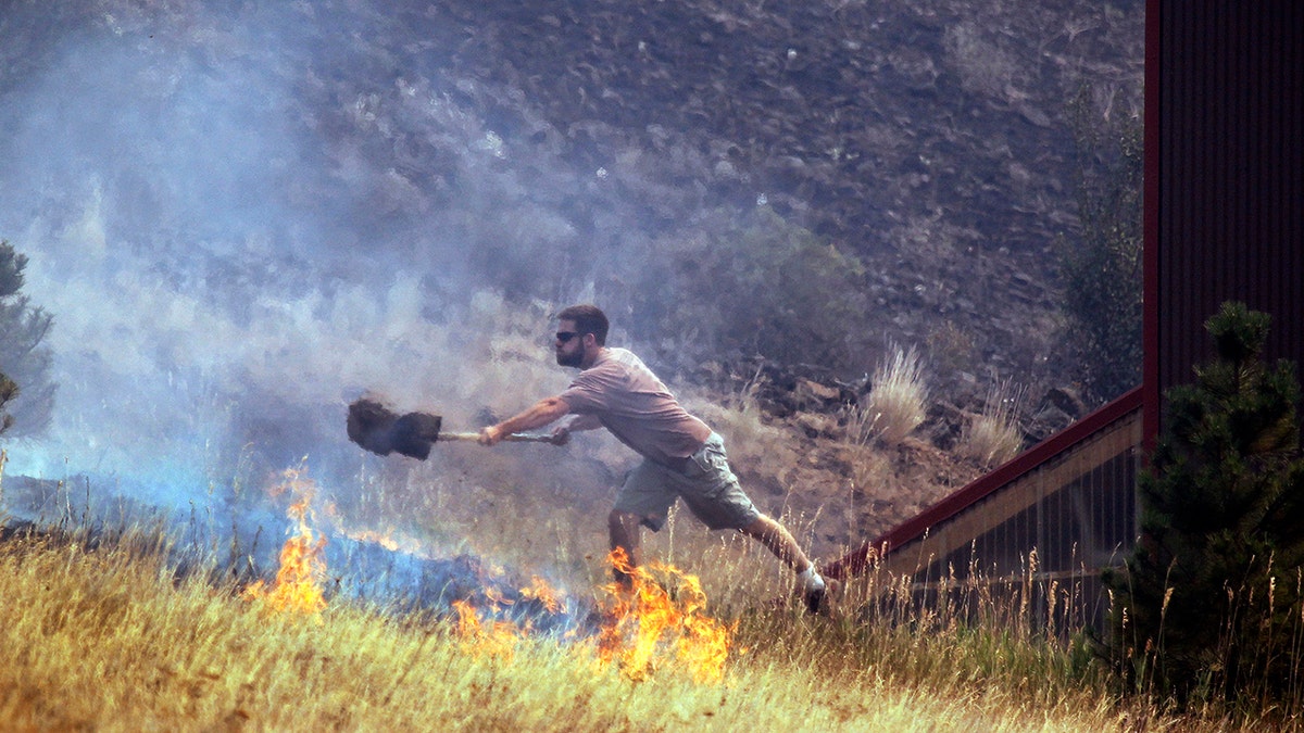 In this Aug. 14, 2012, file photo a man tosses dirt on a fire as he tries to save his home on Bettas Road near Cle Elum, Washington.