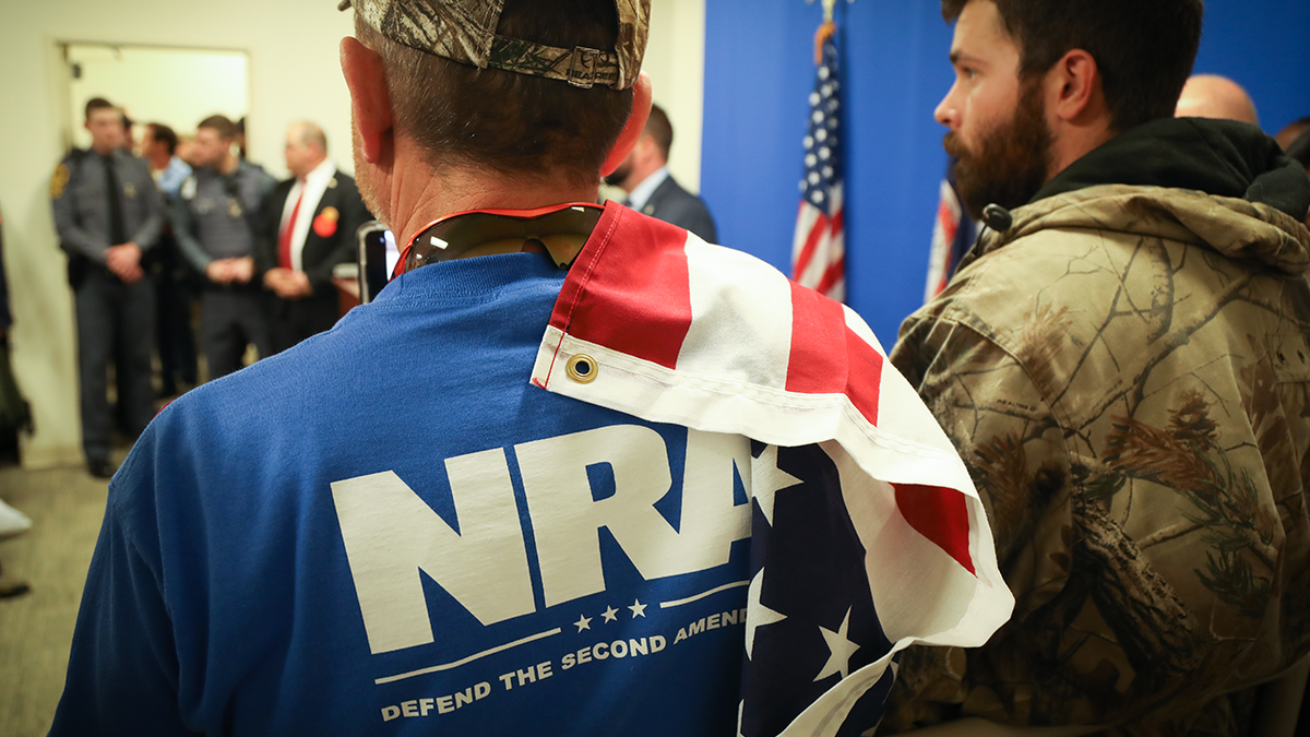 man in blue NRA shirt with US flag draped on shoulder