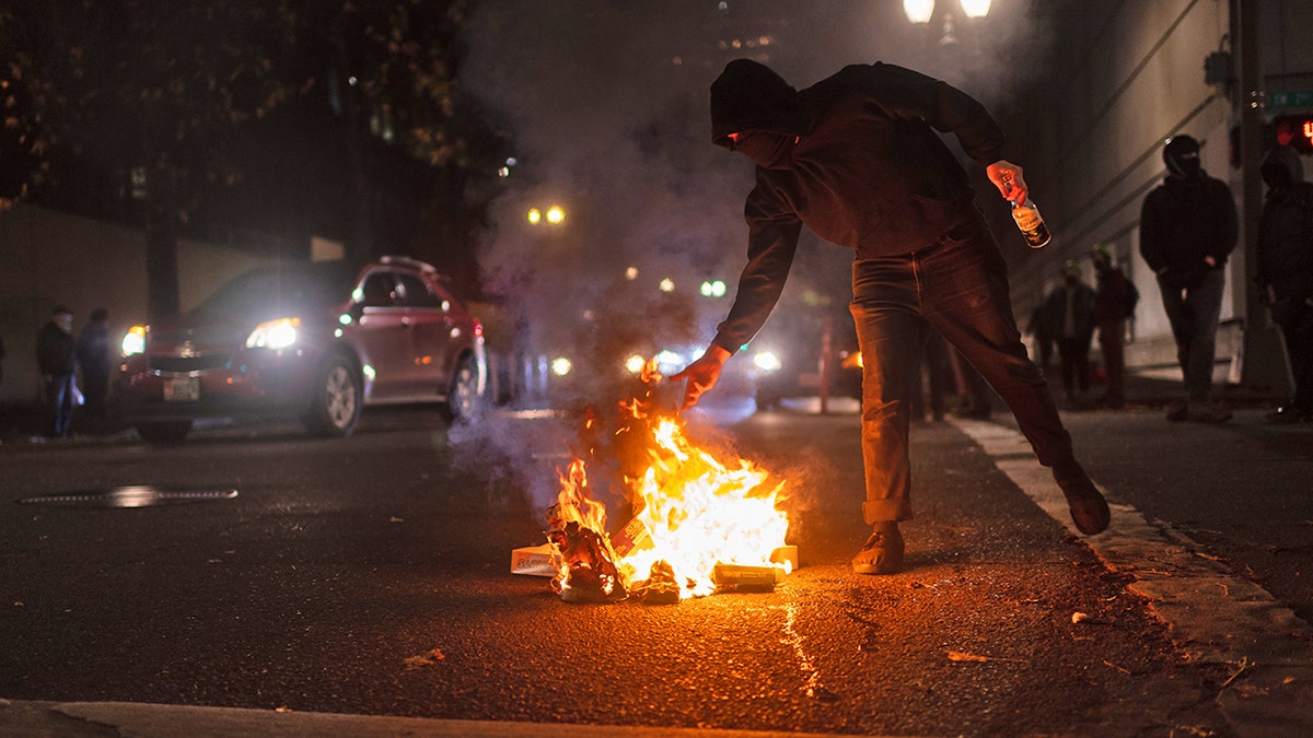 A protester feeds a small fire near the south entrance of the Justice Center after a riot was declared during a protest to decry the verdict in the Kyle Rittenhouse Trial. Portland, Oregon, USA, November 19th, 2021 (Mathieu Lewis-Rolland/SIPA USA)No Use Germany.