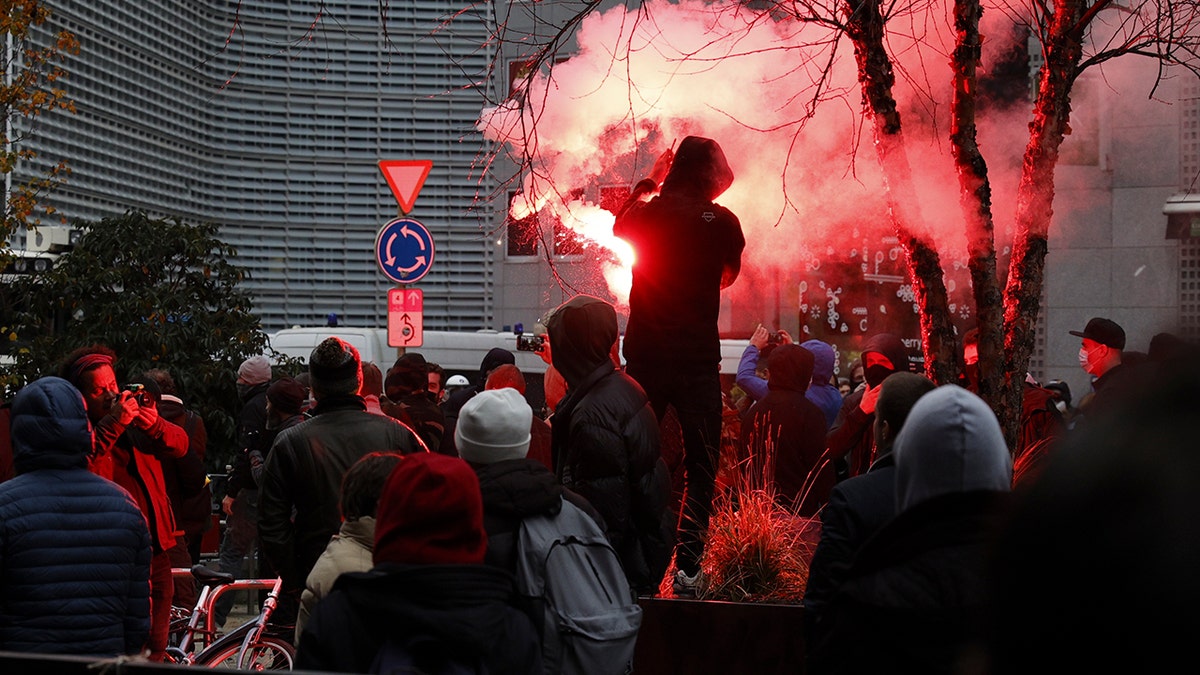 A protester lights a flare during a demonstration against the reinforced measures of the Belgium government to counter the latest spike of the coronavirus in Brussels, Belgium, Sunday, Nov. 21, 2021.