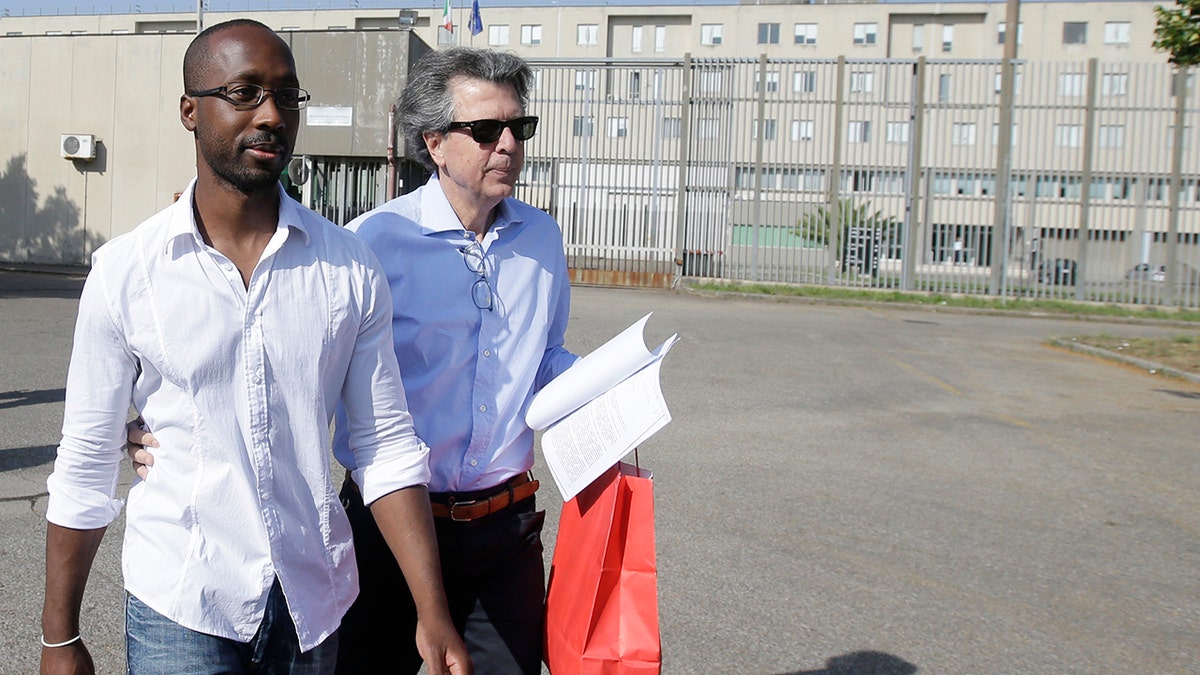 Rudy Guede, left, is greeted by an unidentified person as he leaves the penitentiary for a temporary release of thirty-six hours, in Viterbo, Italy, on June 25, 2016. 