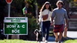 FILE - People walk near one of many signs around town centered around the upcoming Nov. 2 election and equity initiatives in schools in Guilford, Conn., Oct. 19, 2021.  (AP Photo/Jessica Hill, File)
