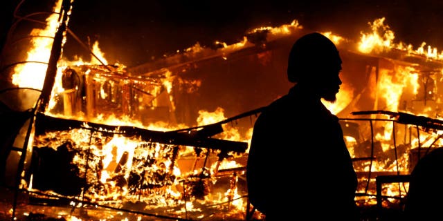 A man watches a burning building after a grand jury returned no indictment in the shooting of Michael Brown in Ferguson, Missouri November 24, 2014.   REUTERS/Jim Young