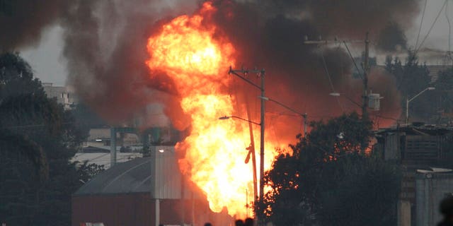 Firefighers and rescue workers stand near a burning gas leak after a series of explosions at a neighborhood in Puebla, Mexico, Sunday, Oct. 31, 2021. Officials say an illegal tap on a gas line is apparently to blame for the early morning explosions that killed at least one person and injured more than a dozen, destroying dozens of homes and causing the evacuation of some 2000 persons. (AP Photo/Pablo Spencer)