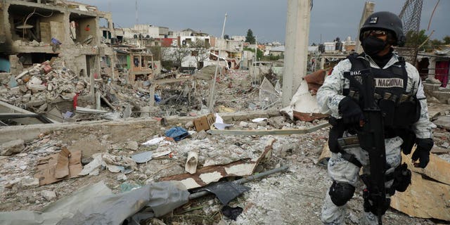 A national guard officer guards the area after a series of explosions at a neighborhood in Puebla, Mexico, Sunday, Oct. 31, 2021. Officials say an illegal tap on a gas line is apparently to blame for the early morning explosions that killed at least one person and injured more than a dozen, destroying dozens of homes and causing the evacuation of some 2000 persons. (AP Photo/Pablo Spencer)