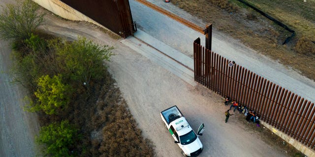 Die texanischen Behörden sagen, dass mindestens 2 Migranten tot und über ein Dutzend verletzt wurden, nachdem sie in einem Waggon „erstickt“ waren 2 DATEI – Ein Grenzschutzbeamter spricht mit Migranten, nachdem sie am 21. März 2021 in Abram-Perezville, Texas, festgenommen und in Gewahrsam genommen wurden. Biden trat sein Amt am 20. Januar an und fast sofort übertraf die Zahl der Migranten die Erwartungen.