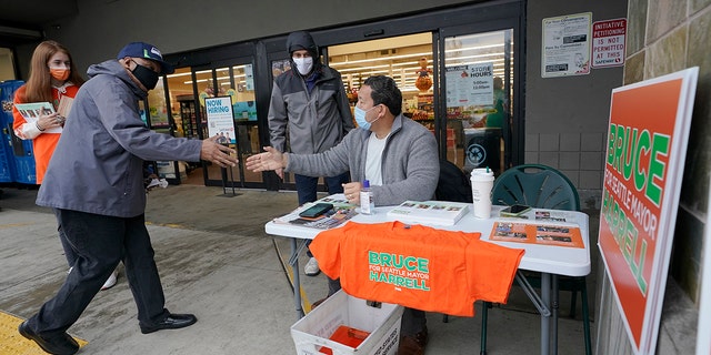 Bruce Harrell, center, shakes hands with shoppers as he campaigns Tuesday, Nov. 2, 2021, on Election Day at a grocery store in South Seattle. (AP Photo/Ted S. Warren)