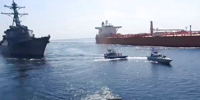 This frame grab from a video released by Iran's paramilitary Revolutionary Guard on Wednesday, Nov. 3, 2021, shows the Guard speed boats, center, in front of a U.S warship, left, amid the seizure of a Vietnamese-flagged oil tanker, right, in the Gulf of Oman. Iran seized the tanker in the Gulf of Oman last month and still holds the vessel, two U.S. officials told The Associated Press on Wednesday, revealing the latest provocation in Mideast waters as tensions escalate between Iran and the United States over Tehran's nuclear program. (Revolutionary Guard via AP)