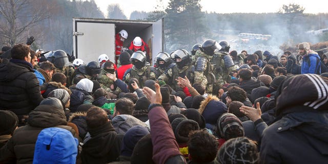 Belarusian servicemen control the situation while migrants get humanitarian aid as they gather at the Belarus-Poland border near Grodno, Belarus, Friday, Nov. 12, 2021.  (Ramil Nasibulin/BelTA pool photo via AP)