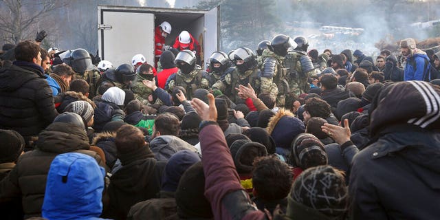 Baltarusijos kariai kontroliuoja situaciją, kai migrantai gauna humanitarinę pagalbą, kai jie renkasi prie Baltarusijos ir Lenkijos sienos netoli Gardino, Baltarusija, penktadienį, 2021 m. lapkričio 12 d. (Ramil Nasibulin / BelTA baseino nuotrauka per AP)