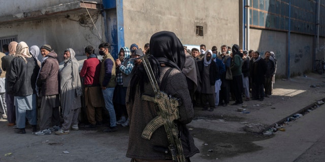 A Taliban fighter secures the area  as people queue to receive cash at a money distribution organized by the World Food Program (WFP) in Kabul, Afghanistan, on Wednesday , Nov. 17, 2021. (AP Photo/ Petros Giannakouris)