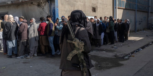 A Taliban fighter secures the area as people queue to receive cash at a money distribution organized by the World Food Program in Kabul, Afghanistan, Nov. 17, 2021.