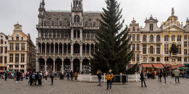 People stand near an undecorated Christmas Tree in Grand Place in Brussels, Friday Nov. 19, 2021. In Brussels the 60-foot Christmas tree was placed in the center of the city's stunning Grand Place on Thursday but a decision on whether the Belgian capital's festive market can go ahead will depend on the development of the COVID-19 virus surge. (AP Photo/Geert Vanden Wijngaert)