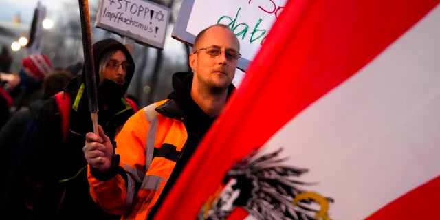 A protestor holds a flare as he walks behind an Austrian national flag during a demonstration against measures to battle the coronavirus pandemic in Vienna, Austria, Saturday, Nov. 20, 2021. Thousands of protesters are expected to gather in Vienna after the Austrian government announced a nationwide lockdown to contain the quickly rising coronavirus infections in the country. Poster in background reads: 'Stop the vaccination fascism'.(AP Photo/Florian Schroetter)