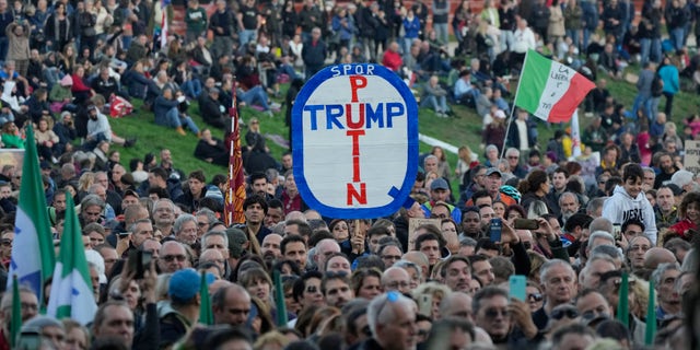 A demonstrator holds a banner reading "Putin, Trump" during a protest against restrictions for the unvaccinated in Rome Circus Maximus, Saturday, Nov. 20, 2021. With infections spiking again despite nearly two years of restrictions, the health crisis increasingly is pitting citizen against citizen — the vaccinated against the unvaccinated. (AP Photo/Alessandra Tarantino)