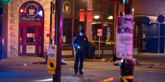 A police officer uses a flashlight while looking for evidence in downtown Waukesha, Wis。, after an SUV sped through a barricade and slammed into a Christmas parade, injuring multiple people Sunday, 11月. 21, 2021. (AP Photo/Jeffrey Phelps)