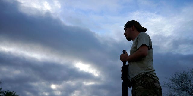 A member of the "Patriots", Will (no last name given), holding his AR-15 rifle, looks across the Rio Grande river on the U.S. - Mexico border as he patrols at sunset outside Brownsville, Texas September 2, 2014. Will is a 25-year-old construction worker from Indiana. The "Patriots" are a heavily armed group who patrol the U.S. border with Mexico, trying to deter immigrants from crossing the border illegally. Photo taken September 2, 2014.